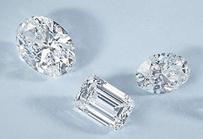 Oval, round, and emerald-cut loose diamonds displayed on a light blue background.