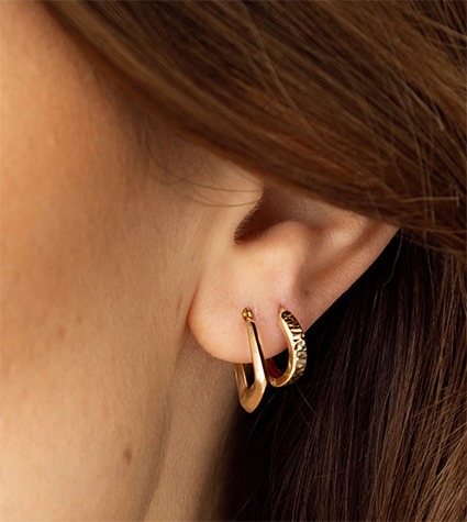 Layered gold huggie hoop earrings on ear
