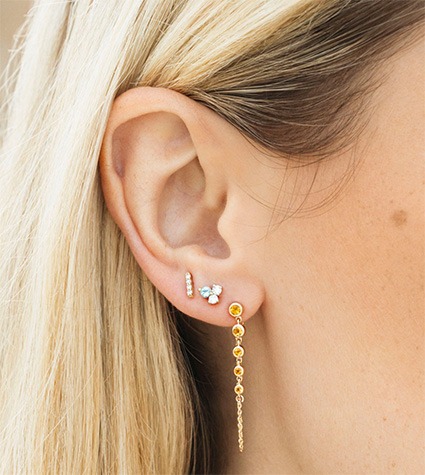 Drop earring paired with gold stud earrings in layered ear styling