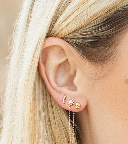 Layered gold stud earrings with starburst and drop chain details in multiple ear piercings