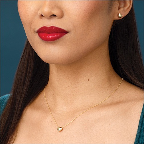 Close up of woman wearing yellow gold chain with puffed yellow gold heart pendant