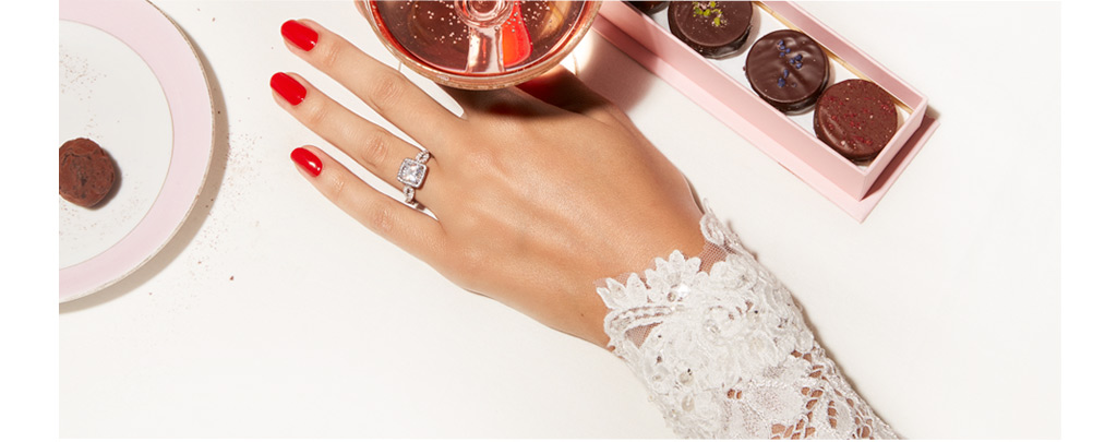 Woman's hand with Kleinfeld diamond engagement ring next to wedding desserts