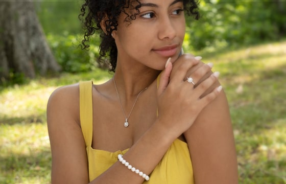 A young woman holding her hand to her shoulder, wearing a pearl bracelet, necklace, and ring.