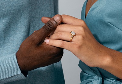 Hands holding an open jewelry box with a completed diamond engagement ring.